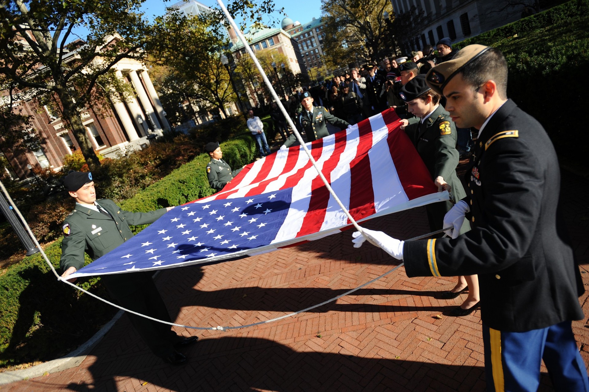 Image of student service members raising American flag up flag pole on campus.