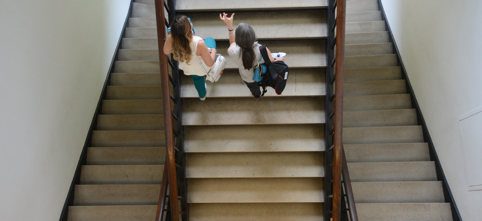 Interior photo of two women walking together up a staircase in Lewisohn Hall while talking.