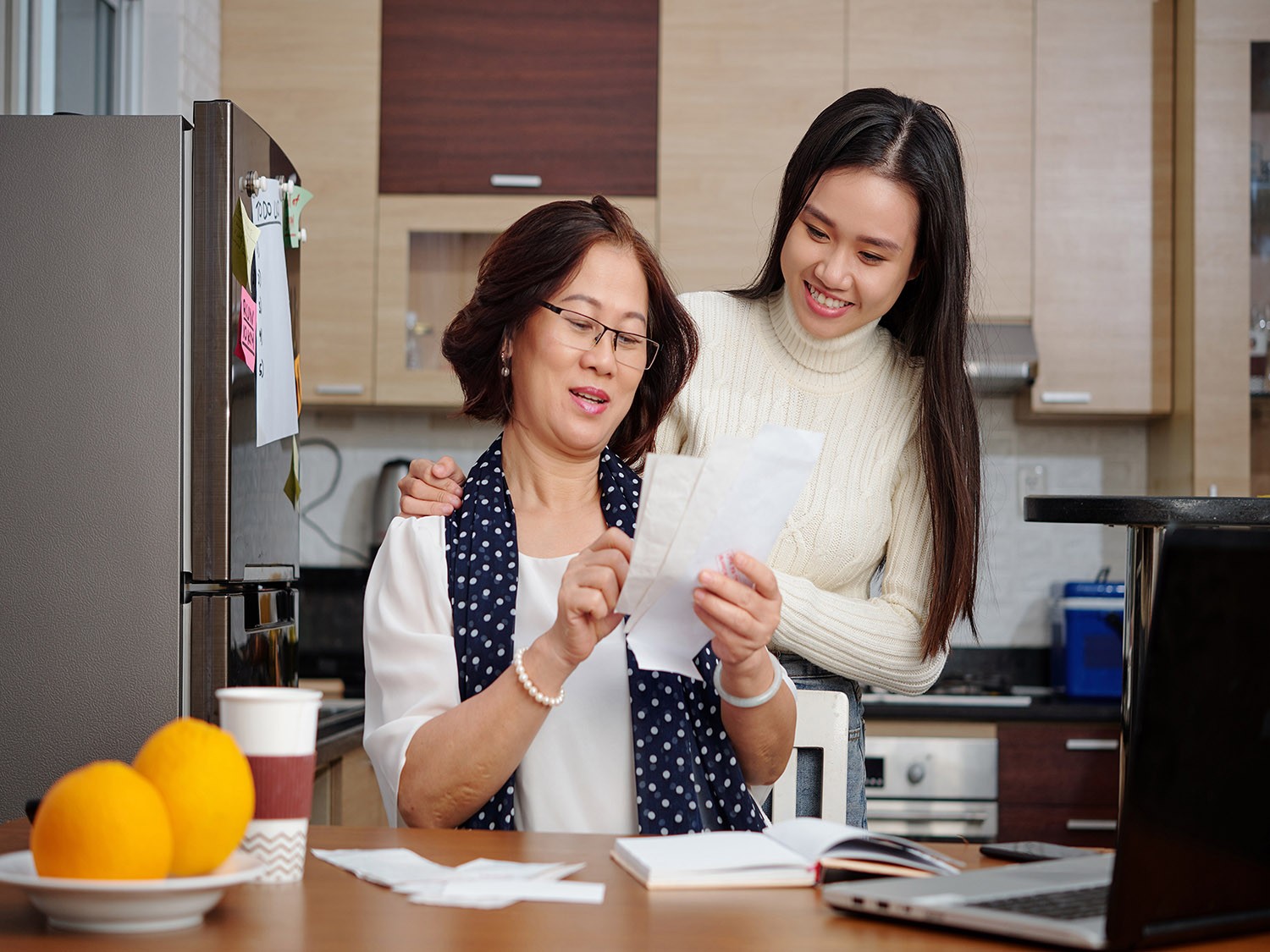 Mother and daughter go over bills together in the kitchen.