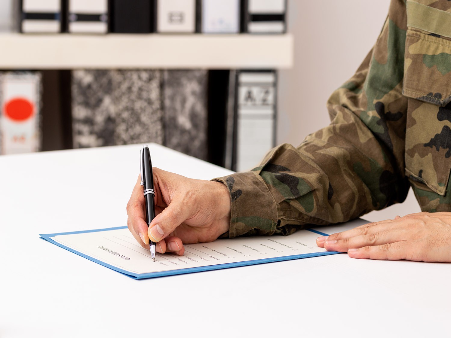 Closeup image of a servicemember signing a document with a pen. 