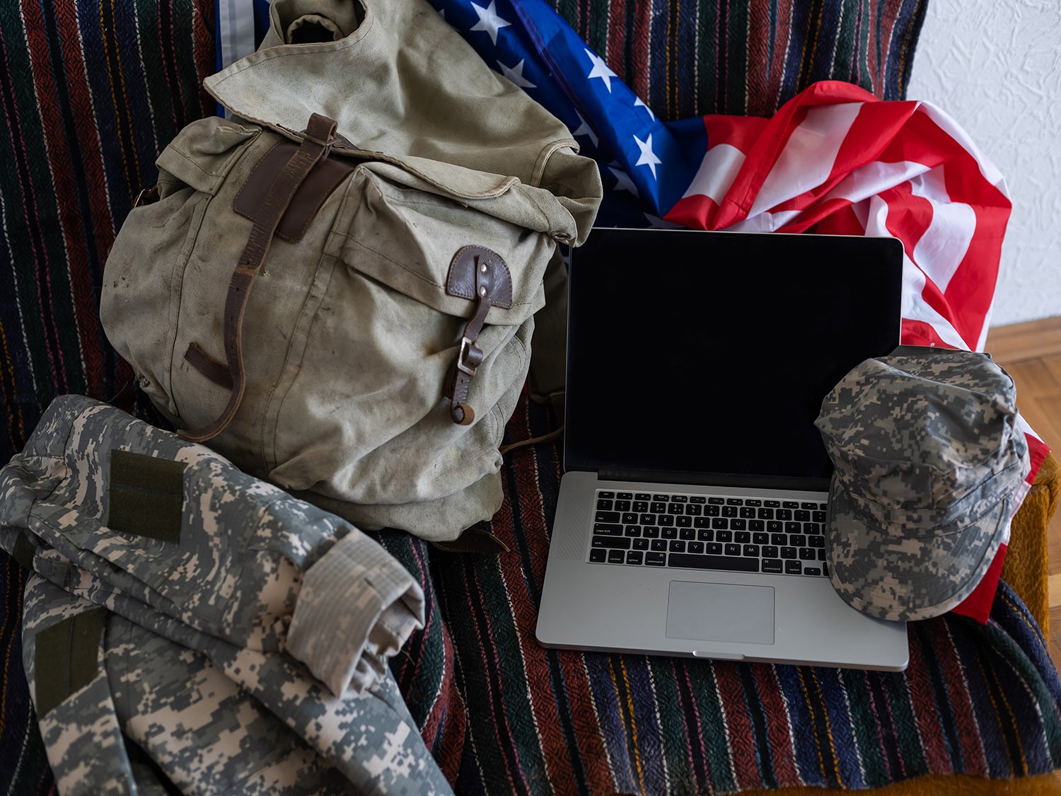 Military backpack next to laptop and American flag.