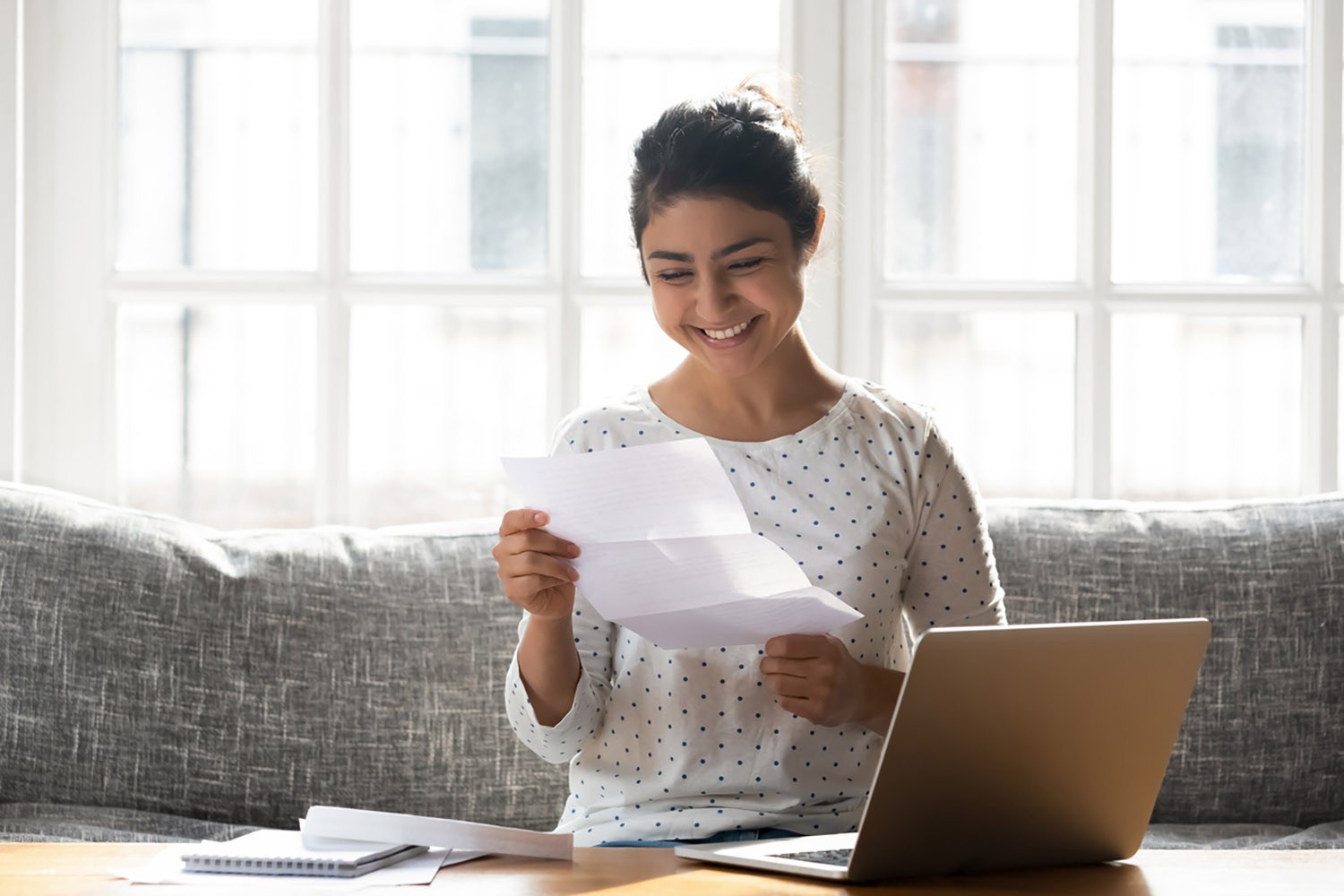 Woman sitting on the couch and smiling while doing paperwork
