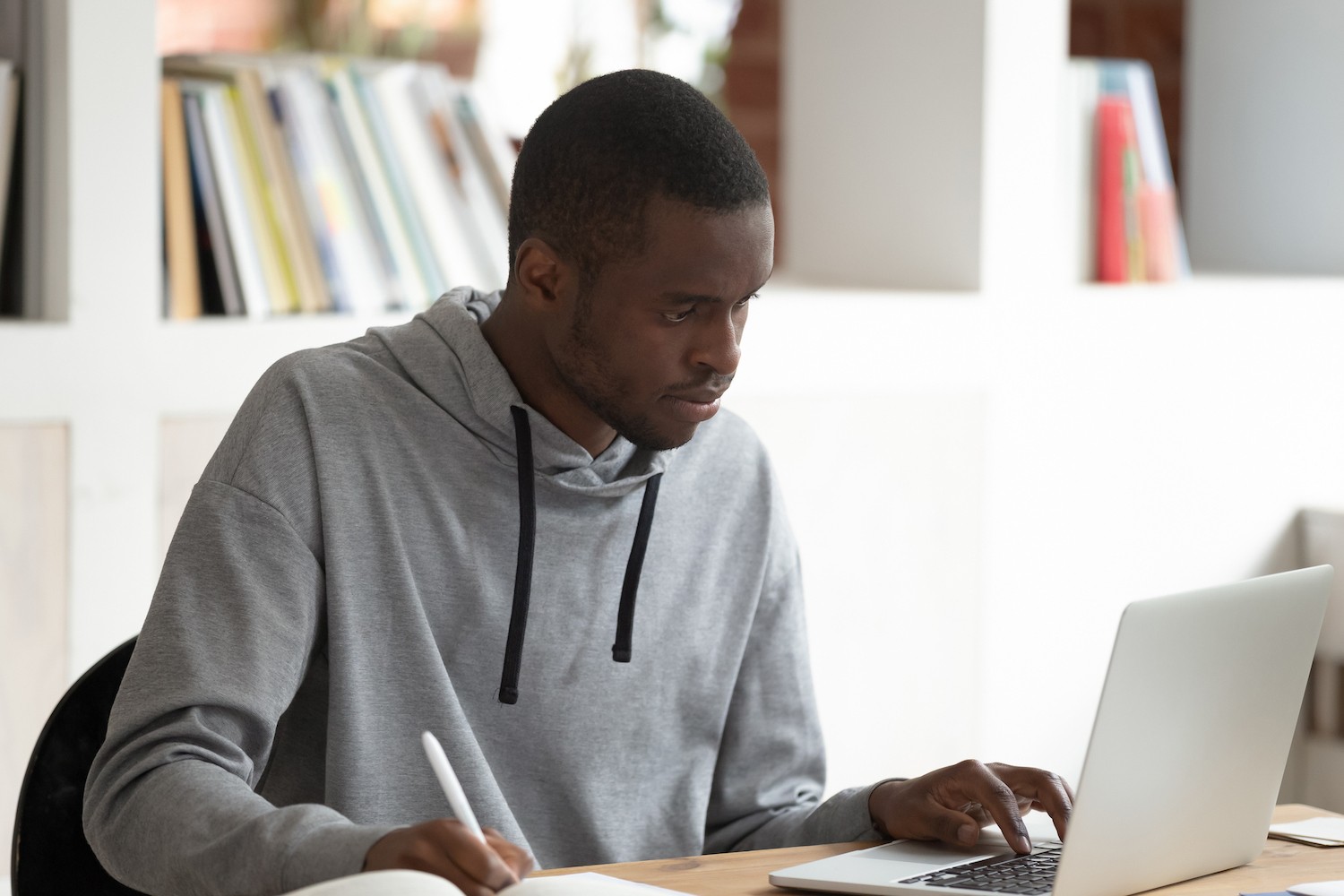 Image of a young black man working at a computer and writing with a pen.