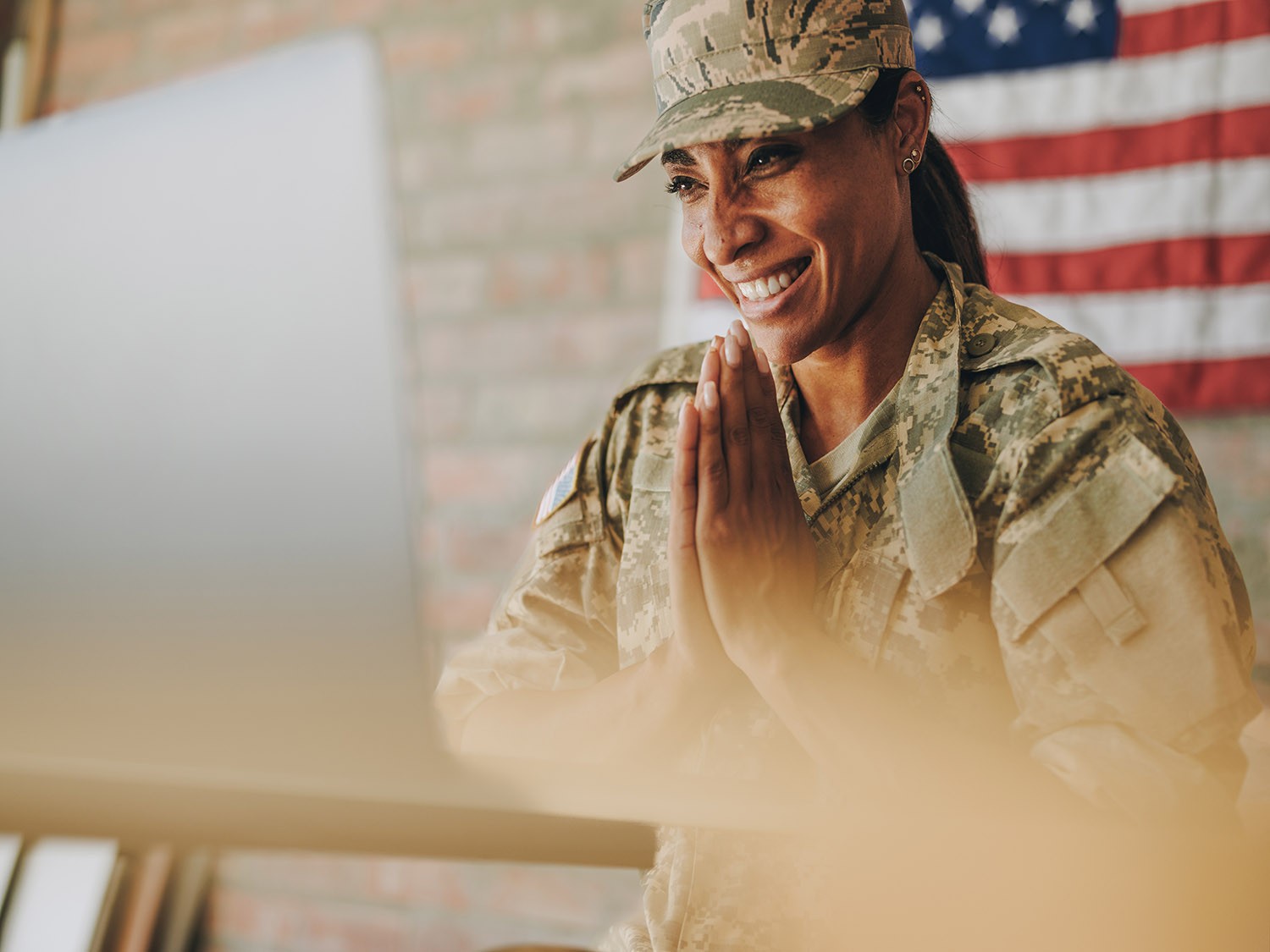 Servicewoman talking with loved ones over video call in front of an American flag. 